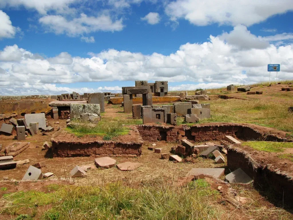 Široki panoramski pogled na arheološko nalazište Puma Punku sa razbacanim megalitskim ruševinama i geometrijski oblikovanim kamenim blokovima pod plavim nebom