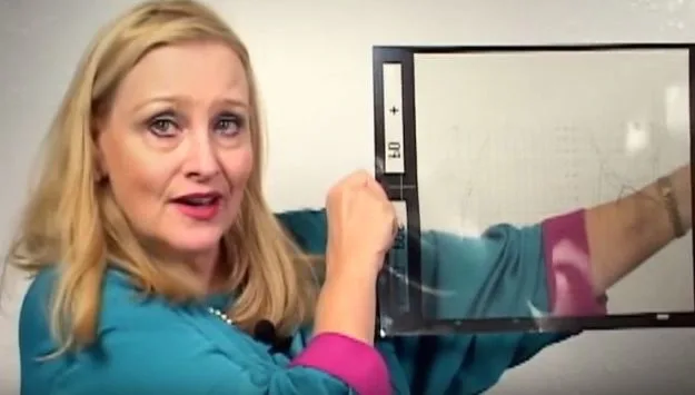 Donna Hare drži prozirnu foliju s tehničkim grafikonima dok govori pred kamerom.